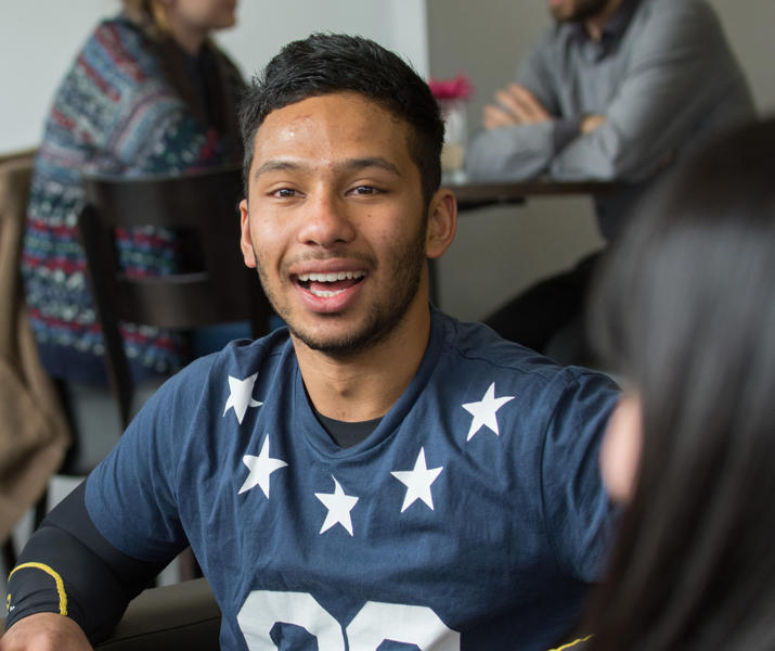Imager of international student sat with a group of people at a table in the lounge 