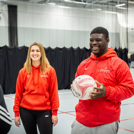 Image of two Hartpury students smiling in a sports hall, with one student holding a football