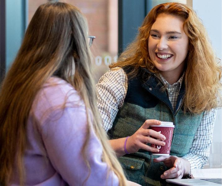 Image of two students sat happily at a table with a hot drink