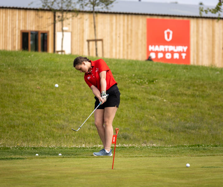 Female Student Practising In Short Game Golf Area