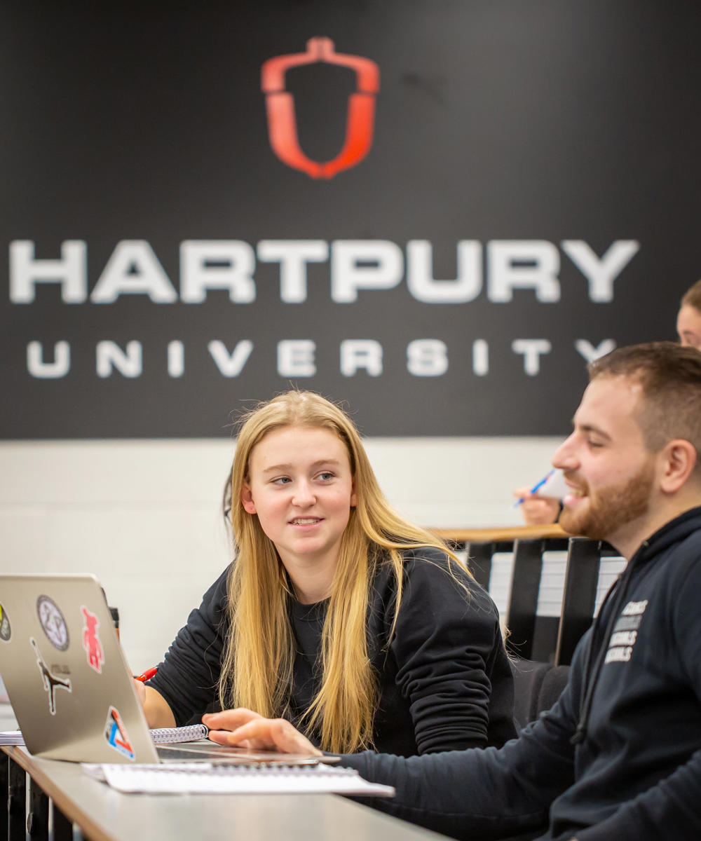 Image of students sat in a lecture theatre with their laptop and notepad