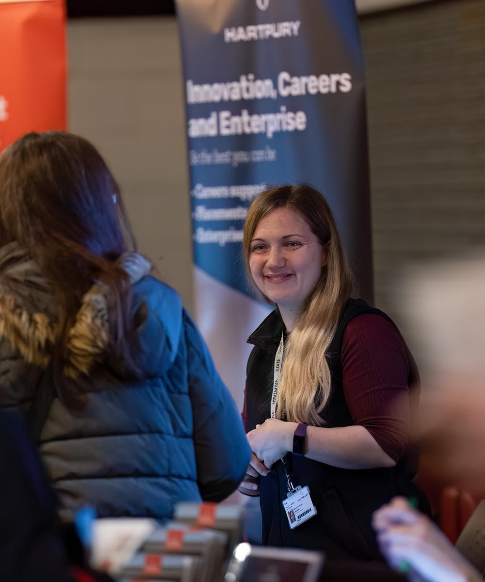 Image of staff member from support team smiling at guest at an open day